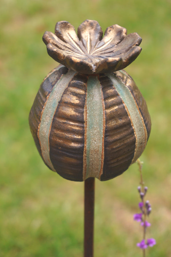 Ceramic poppy seed head garden ornament with bronze glaze catching the sunlight